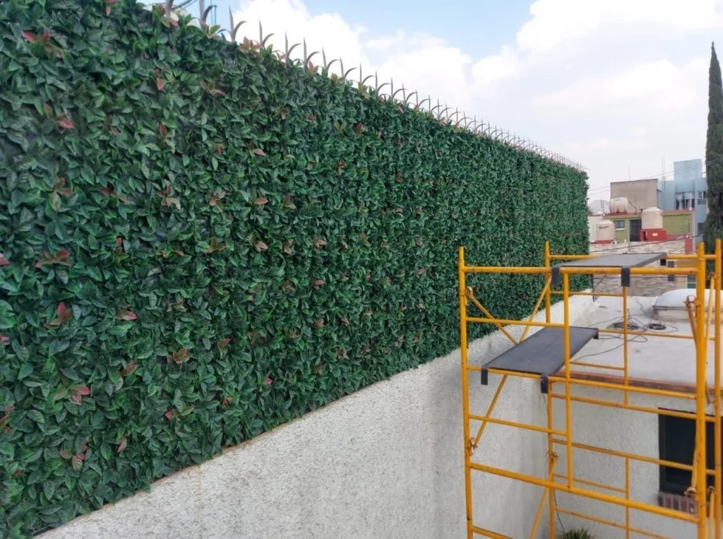 Instalación de follaje artificial sobre una barda con andamio.